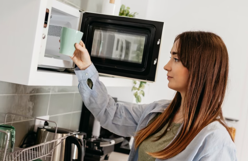 Casual girl using microwave to heat cup
