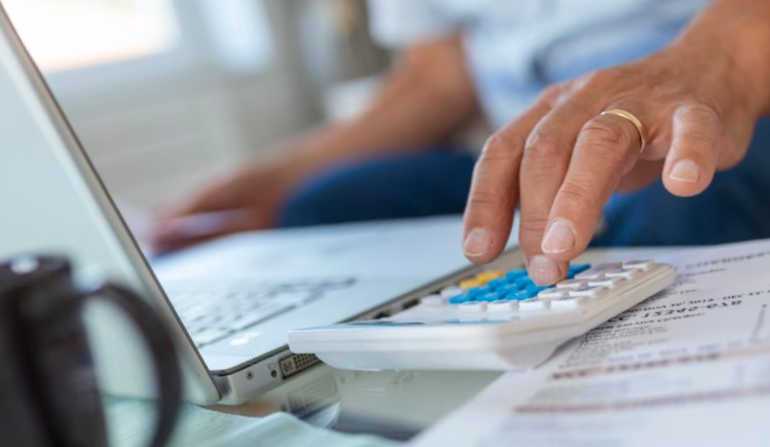 Serious elder senior greyhaired grandpa using calculator counting bank loan payment holding papers at home focused 
