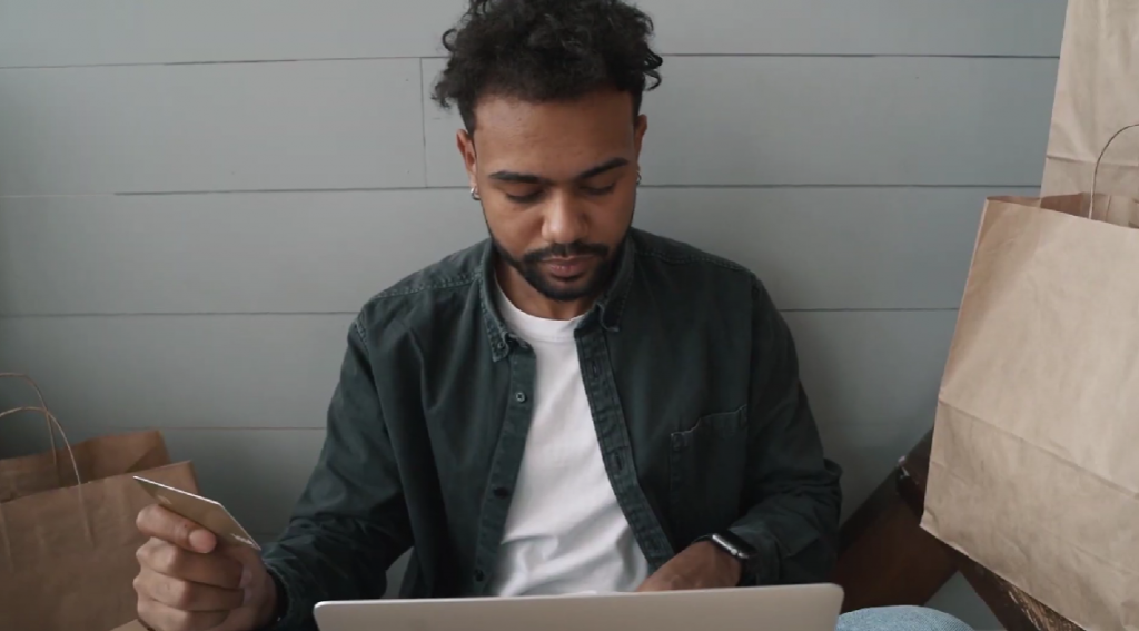 man of color in front of laptop with credit card in hand